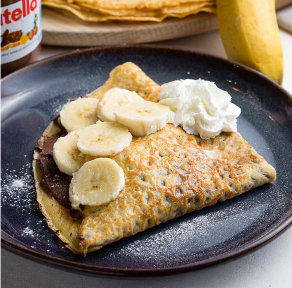A Nutella and banana crêpe with whipped cream and icing sugar