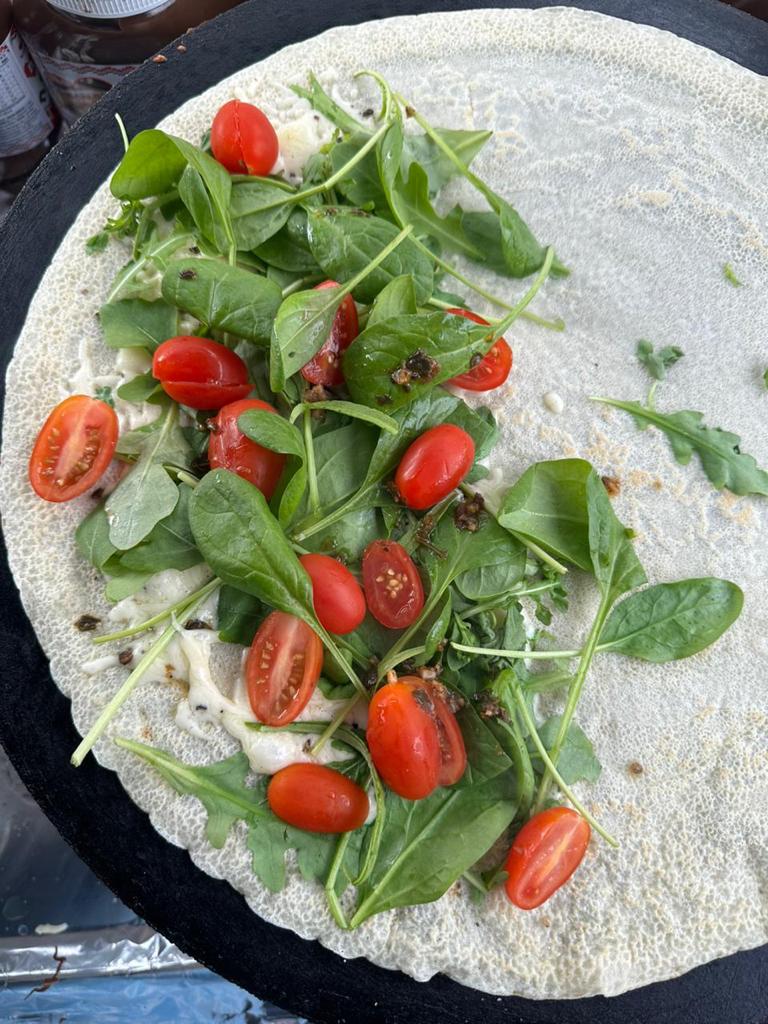 A crêpe on the hot plate topped with baby spinach, rocket and cherry tomatoes