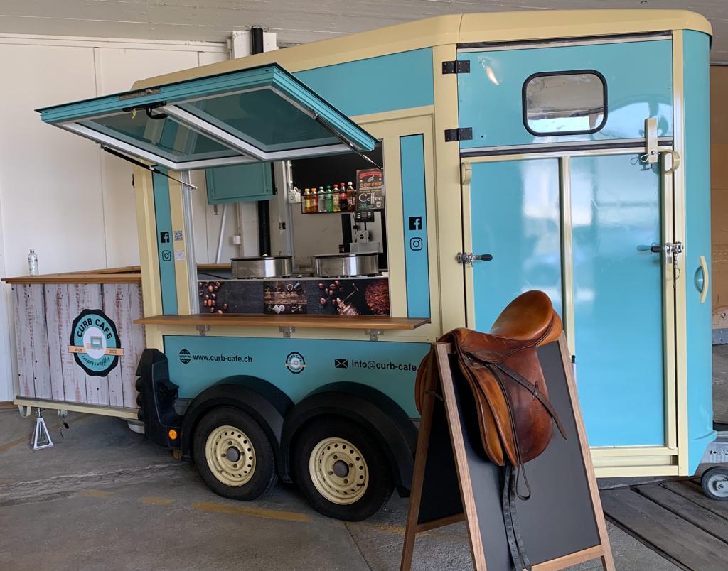 The Curb Cafe trailer, a converted turquoise horse trailer, with a saddle on the chalkboard stand